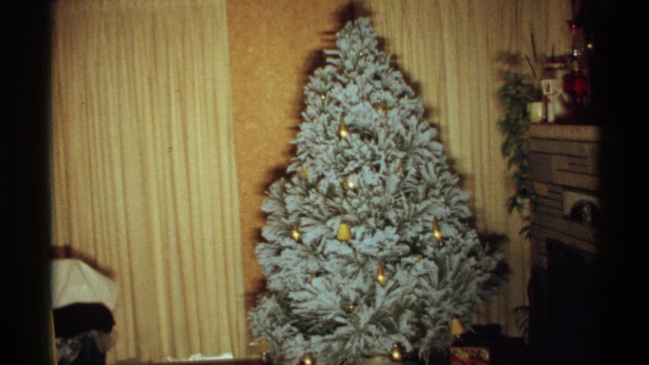 Flocked Christmas tree centered between curtains and a fireplace mantel in a living room.