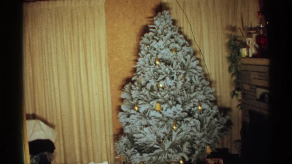 1971 Wisconsin frame of a flocked Christmas tree with ornaments, lights, curtains, and mantel decor.