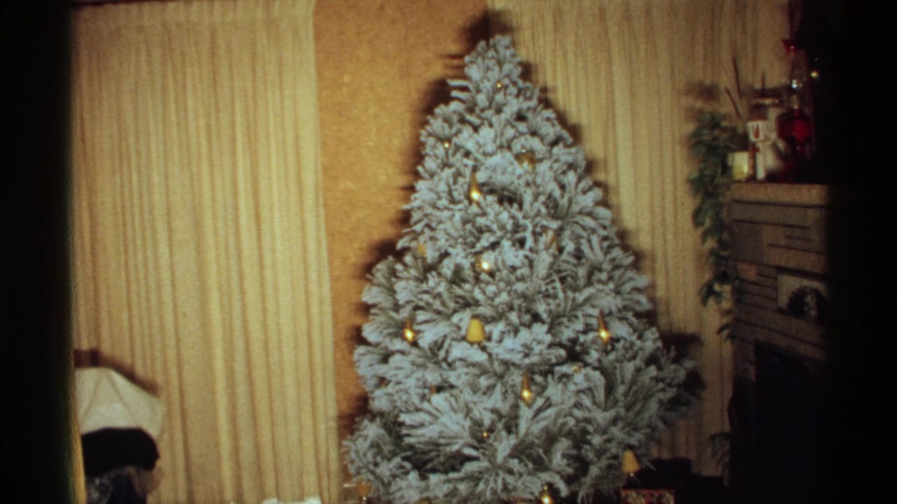 Indoor flocked Christmas tree with ornaments, curtains, and fireplace detail.