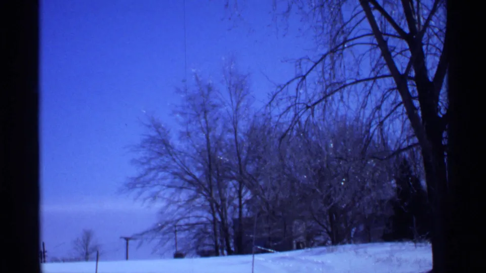 Wisconsin winter home-movie frame showing snow-covered ground, bare trees, and a clear blue sky after the date card.