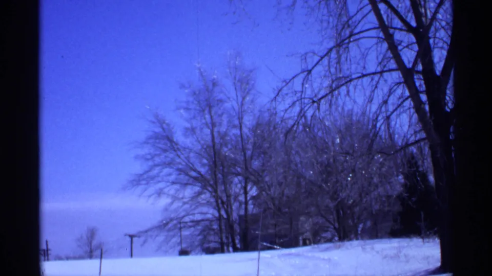 Blue-tinted 8mm frame of a snow-covered Wisconsin landscape with leafless trees and a quiet open foreground.