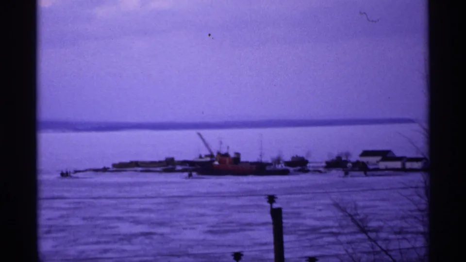 Ashland, Wisconsin winter waterfront in 1971, with boats or barges along frozen water under a muted sky.