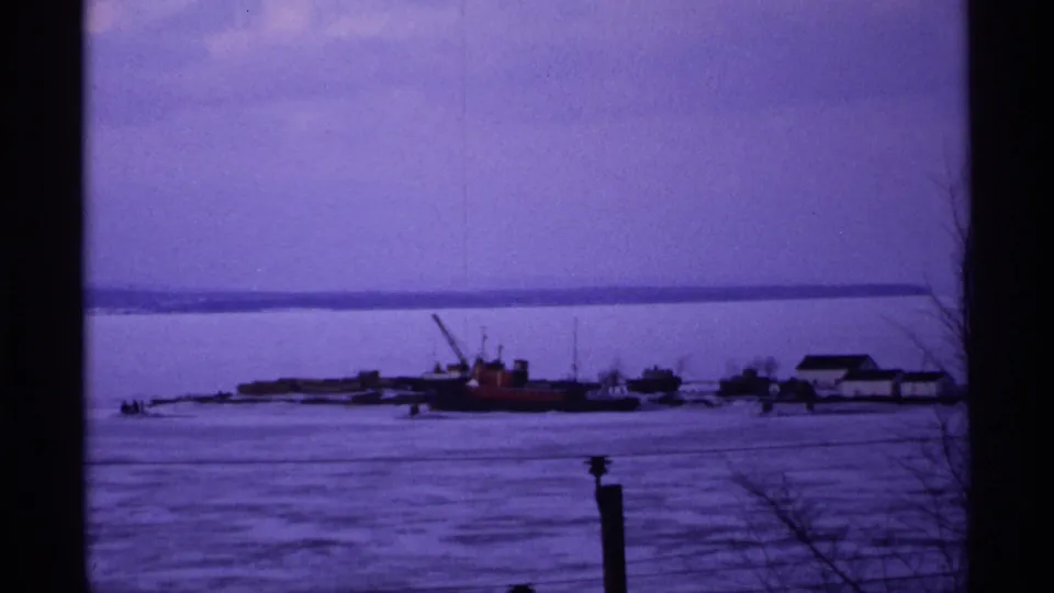 Wide 1971 Ashland waterfront view across frozen water, with industrial-looking boats and low buildings on shore.