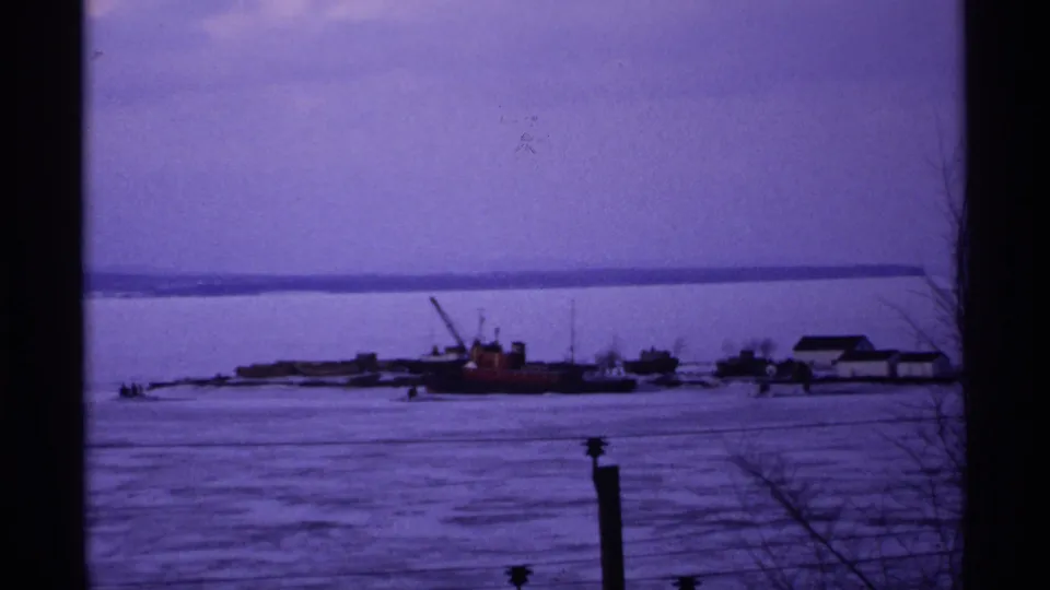 End frame of the 1971 Ashland winter waterfront, showing boats near low shoreline buildings across frozen water.