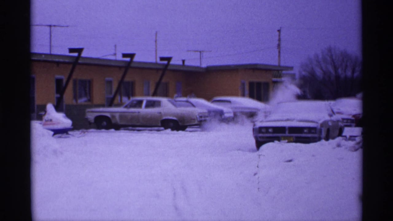 Snow-covered motel parking lot with parked cars and a low building behind them.