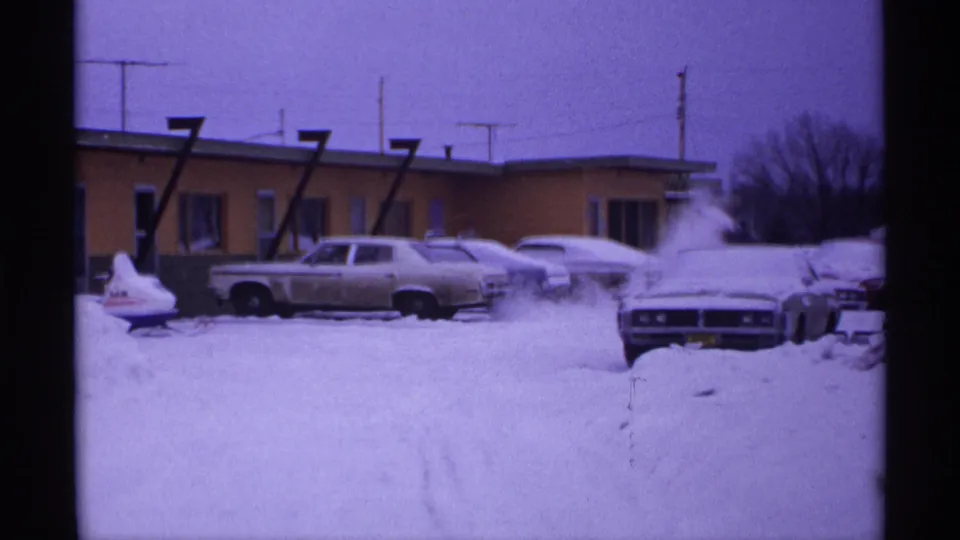 1971 Wisconsin 8mm frame showing snowbound cars in a motel parking lot with large numeral signs on the building.
