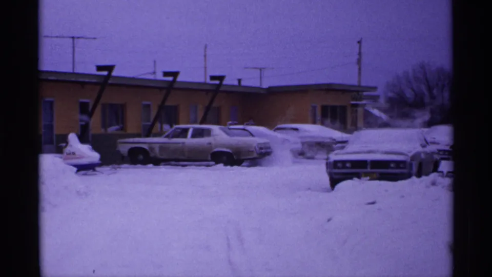 1971 Wisconsin winter frame with cars surrounded by snow in front of a motel building under a purple-tinted sky.