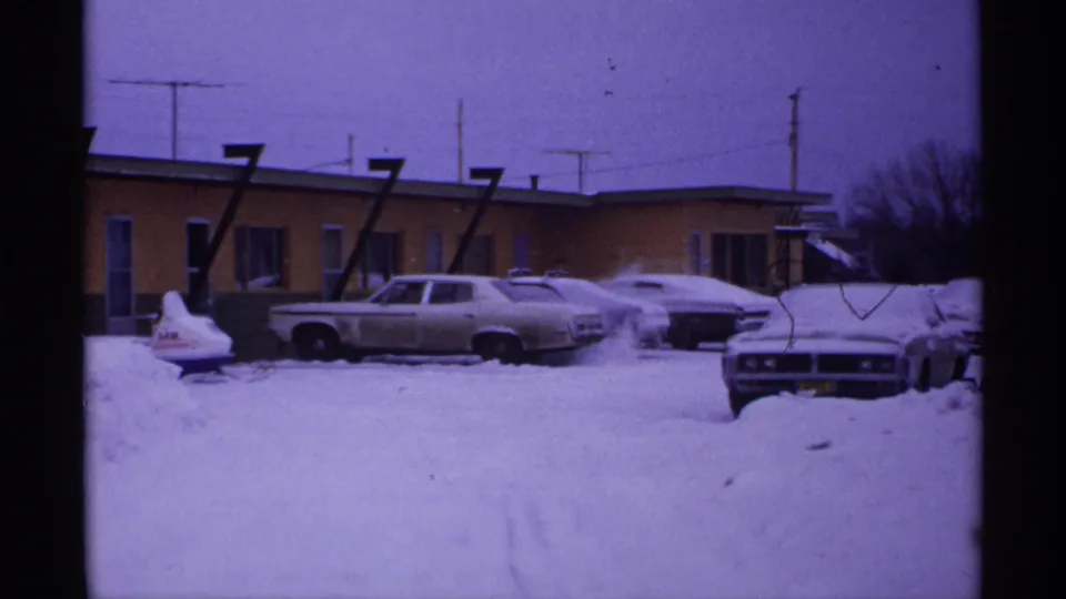 1971 Wisconsin 8mm view of a motel parking lot where cars and a small snowmobile-like object are partly buried in snow.