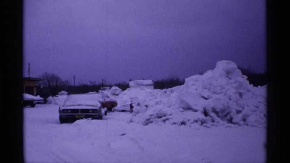 1971 Wisconsin 8mm frame showing parked cars partly buried by heavy snow beside a large plowed snowbank.