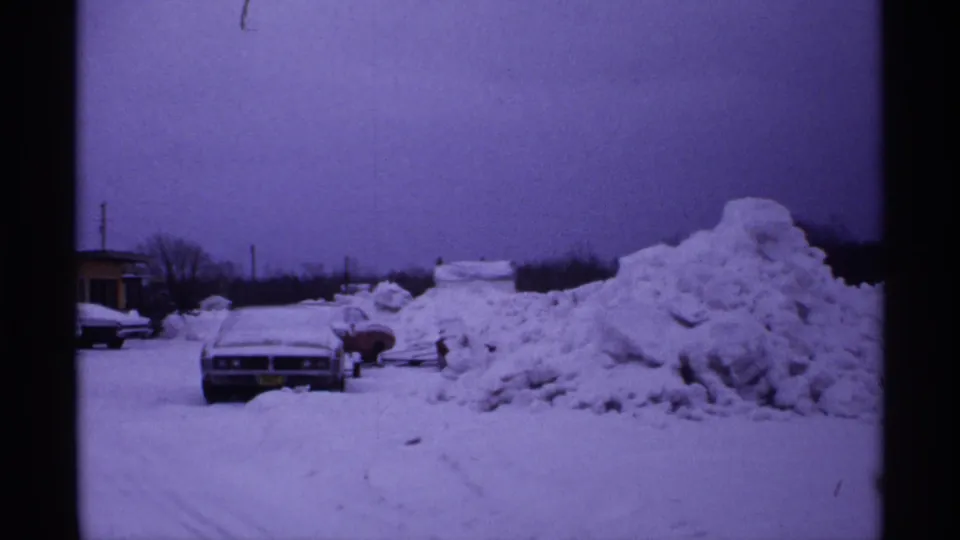 1971 Wisconsin winter frame with a parked sedan facing the camera and deep plowed snow along the roadside.
