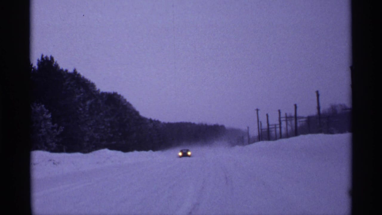 Distant car headlights on a snow-covered rural road during heavy snowfall.