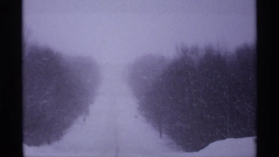 The 8mm footage shows a snow-covered rural road receding between wooded edges in Wisconsin winter weather.