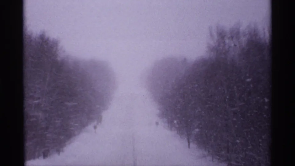 1971 home-movie frame of a narrow snowy road through trees in the Ironwood, Michigan sequence.