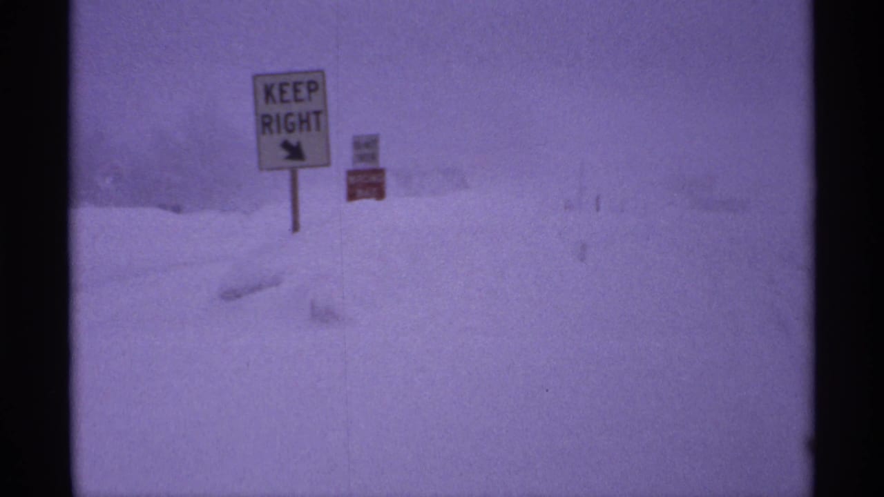 Snow-covered Ironwood-area roadside with a KEEP RIGHT traffic sign visible through falling snow.