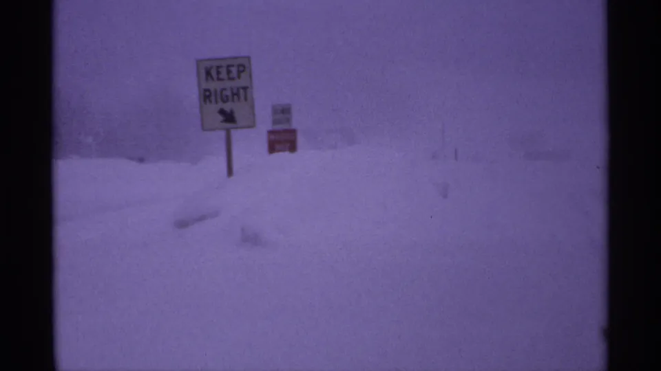 Vintage 8mm view of a KEEP RIGHT traffic sign near a snow-buried roadside in winter weather.