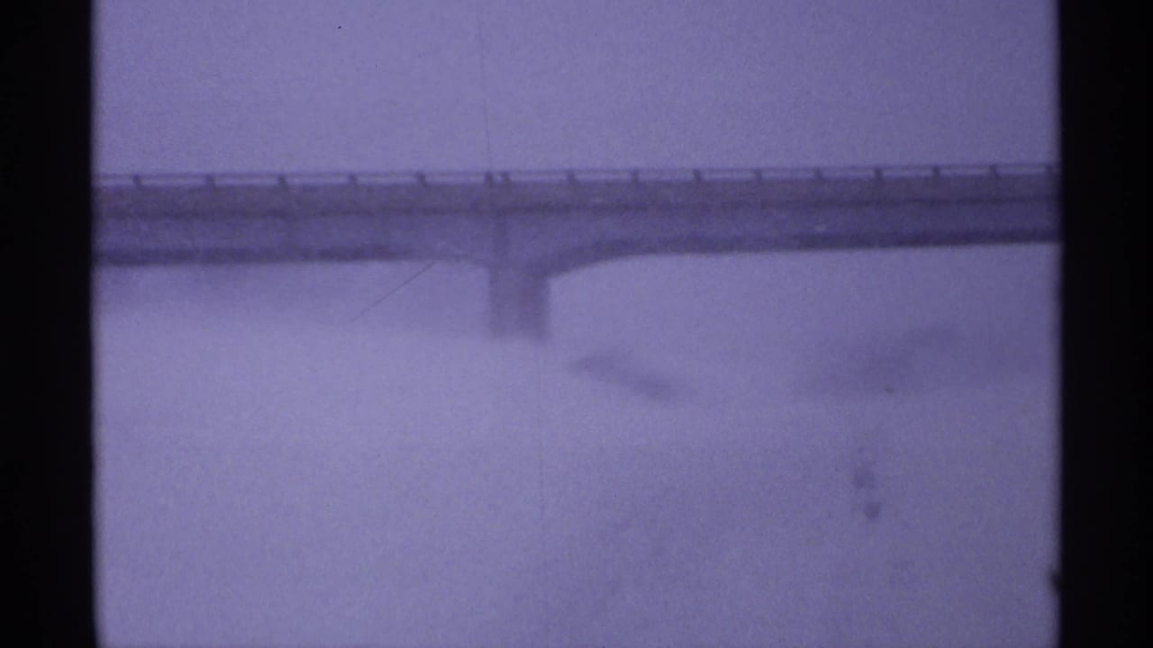 A distant overpass cuts across a pale snowy Wisconsin landscape, softened by 8mm grain and winter haze.