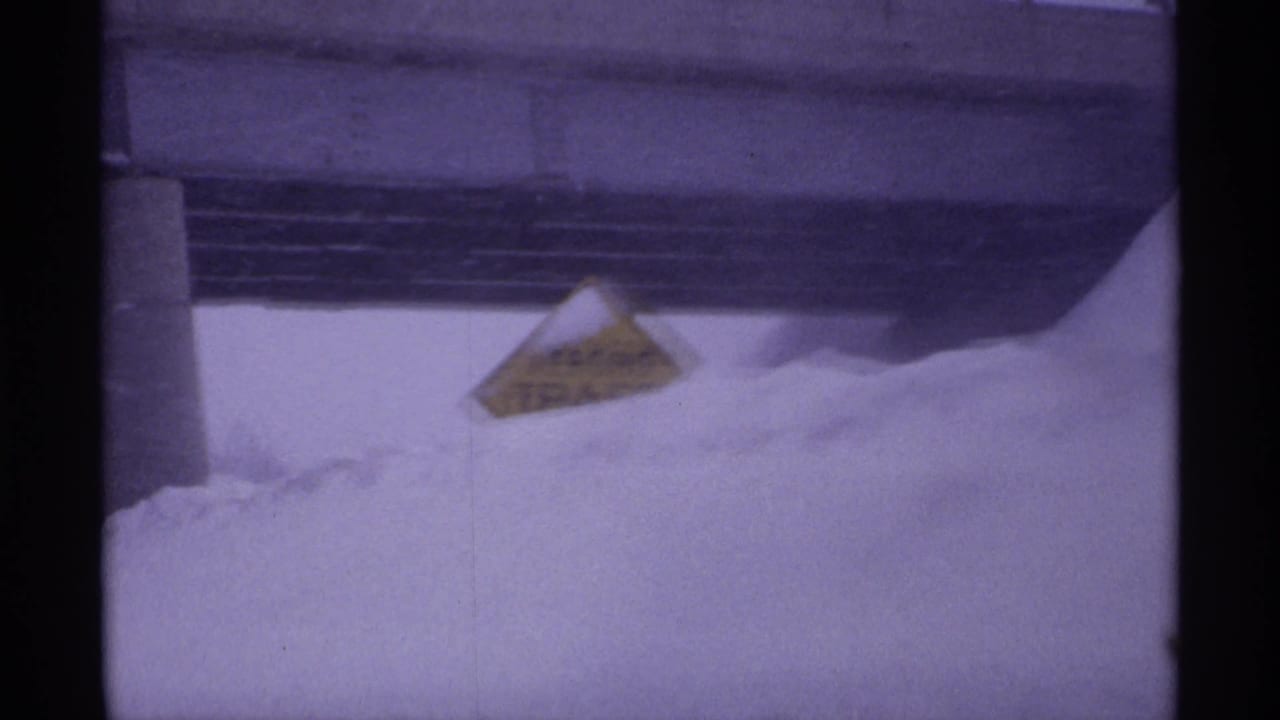 Snowbank beneath an overpass with a yellow roadside warning sign protruding from the snow.