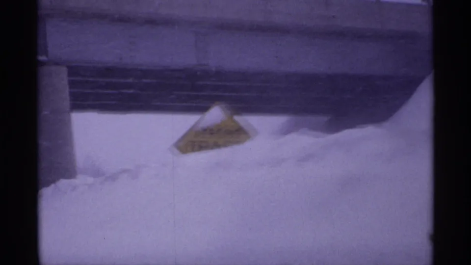 1971 Wisconsin winter frame with a yellow roadside warning sign emerging from deep snow below an overpass or bridge.