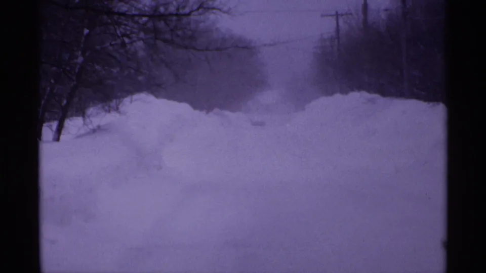 1971 Wisconsin 8mm view down a snow-covered road with high plowed banks, bare trees, and utility lines in winter haze.