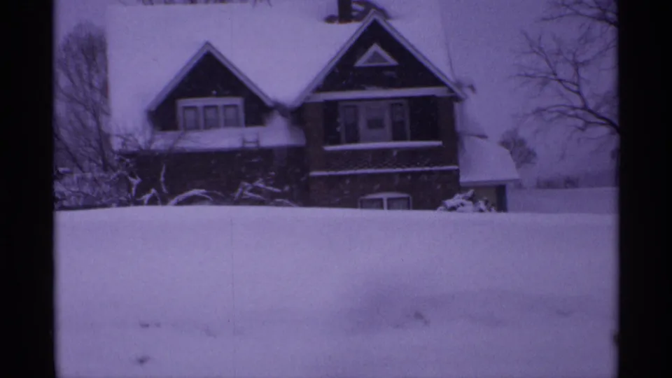 1971 Wisconsin frame showing a steep-roofed residential house behind a snow-covered yard, with bare winter trees and purple 8mm film color.