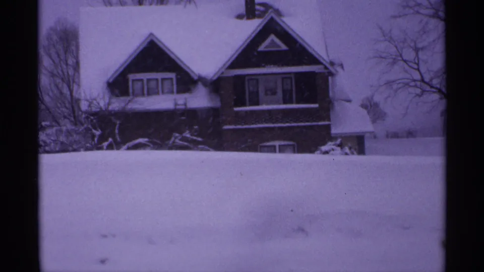 1971 Wisconsin home-movie frame of a two-story house with snow on the roof and a high snowbank in the foreground.
