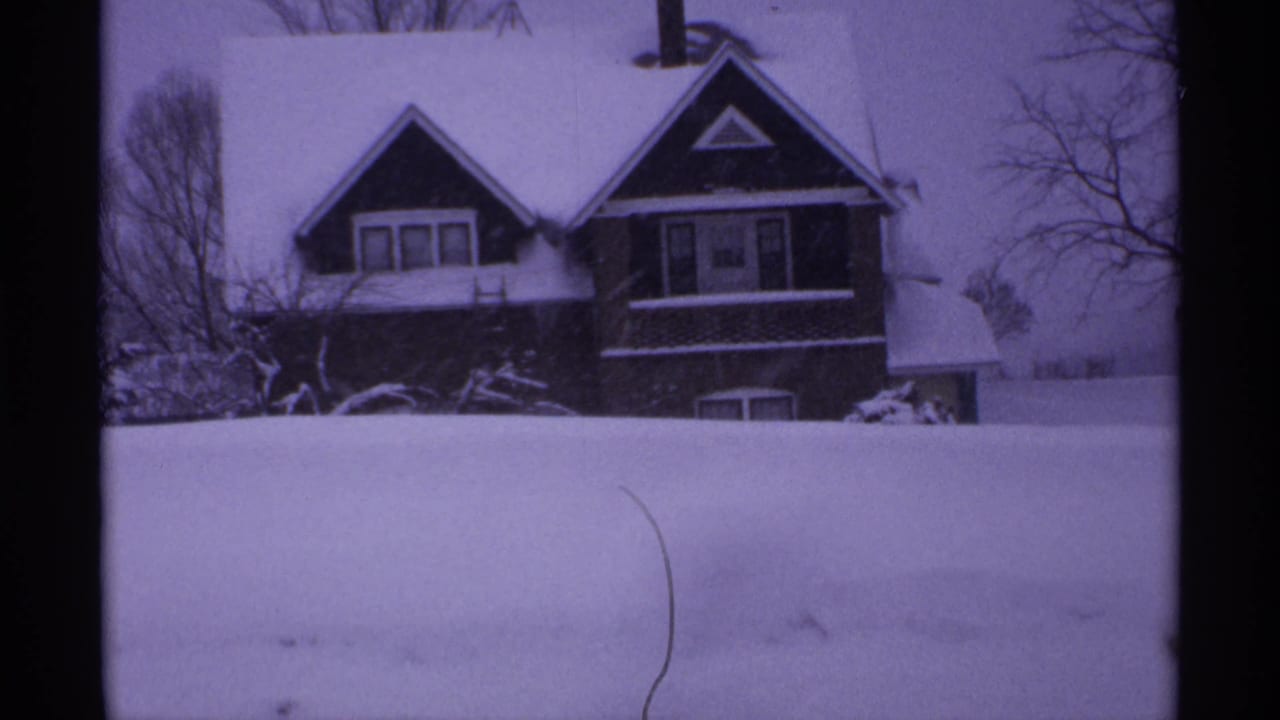 1971 Wisconsin frame showing a snow-covered house behind a broad drift, with leafless trees around the property.