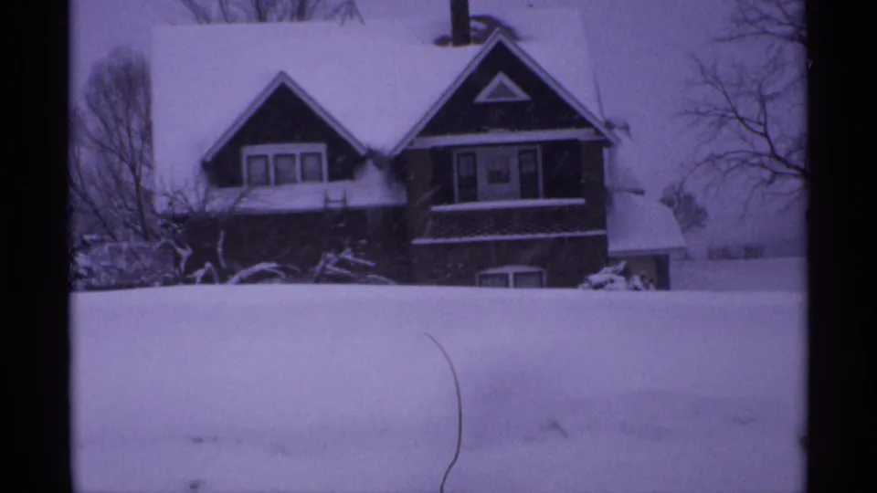 1971 Wisconsin frame showing a snow-covered house behind a broad drift, with leafless trees around the property.