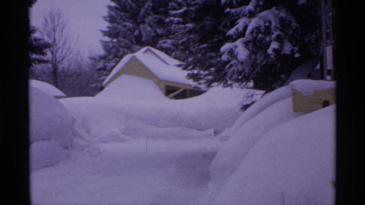 1971 Wisconsin 8mm frame showing deep snow piled around small homes and snow-laden evergreens.