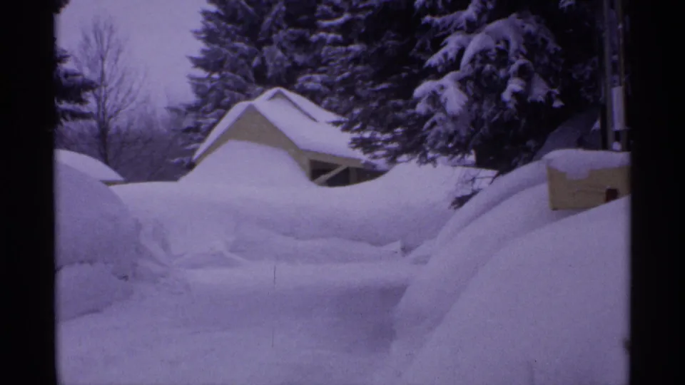 1971 Wisconsin 8mm frame showing deep snow piled around small homes and snow-laden evergreens.