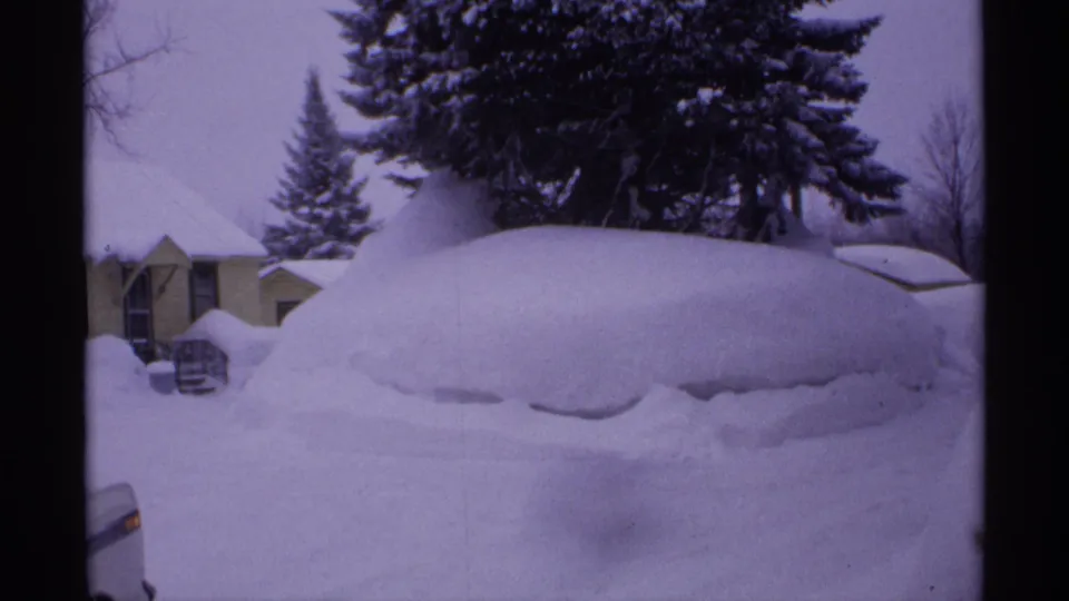 1971 Wisconsin 8mm view of a residential property with a car and house largely obscured by accumulated snow.