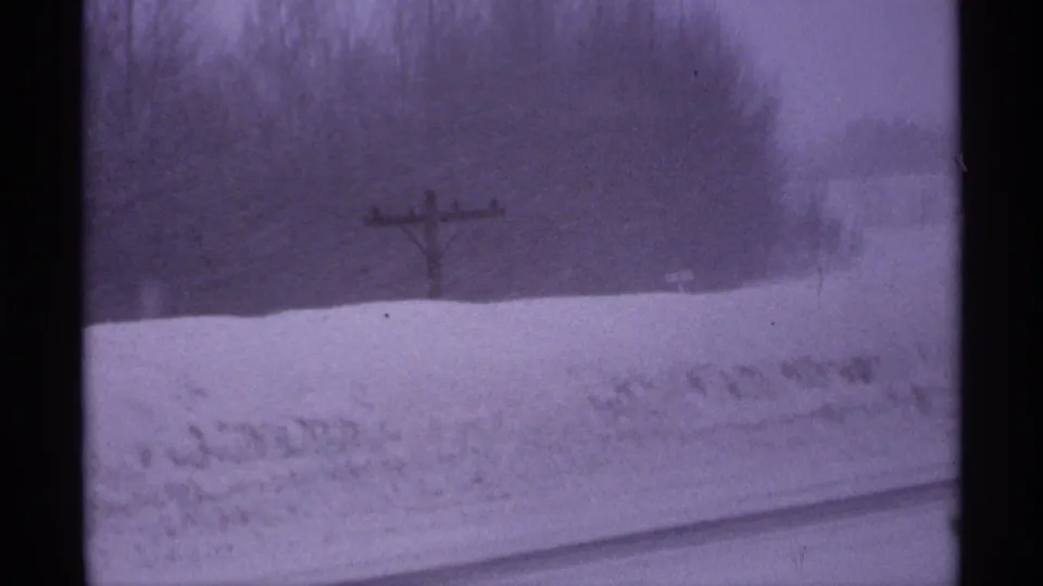 1971 Wisconsin 8mm frame showing a snow-covered rural roadside, wooden utility pole, bare trees, and dark film edge.