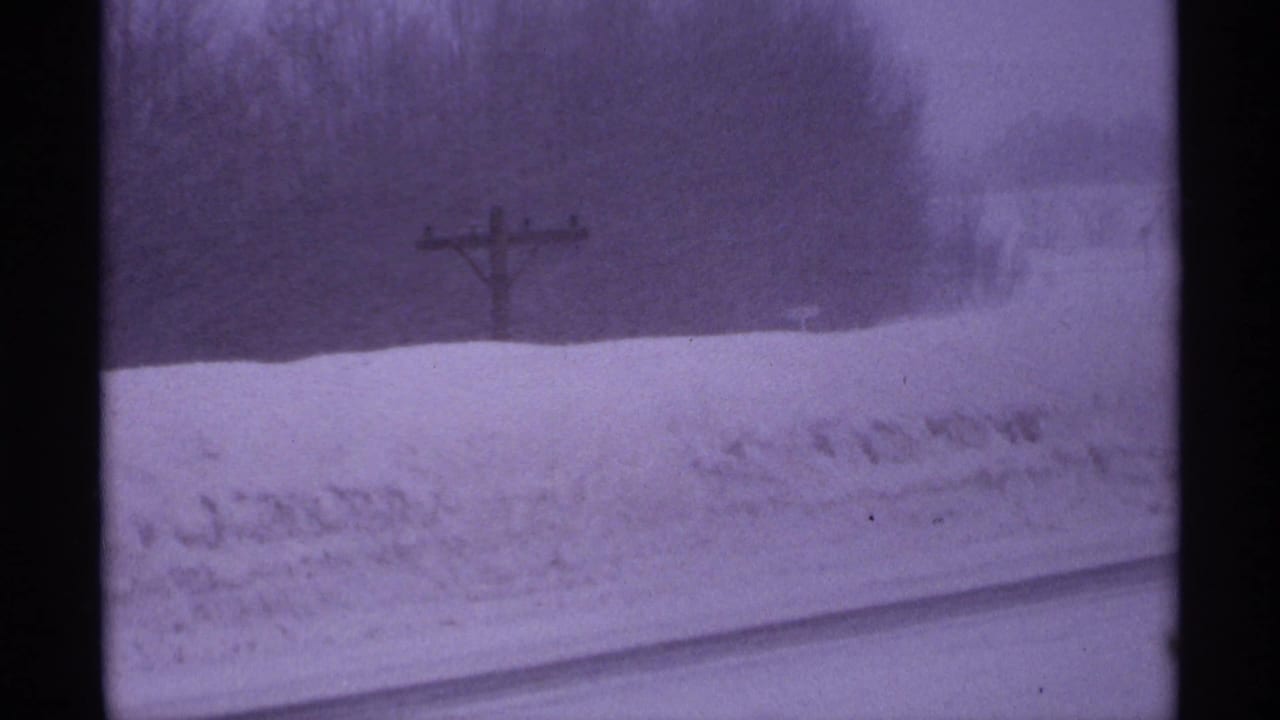 1971 Wisconsin home-movie frame with snowbanks, a wooden utility pole, distant trees, and visible film gate edges.