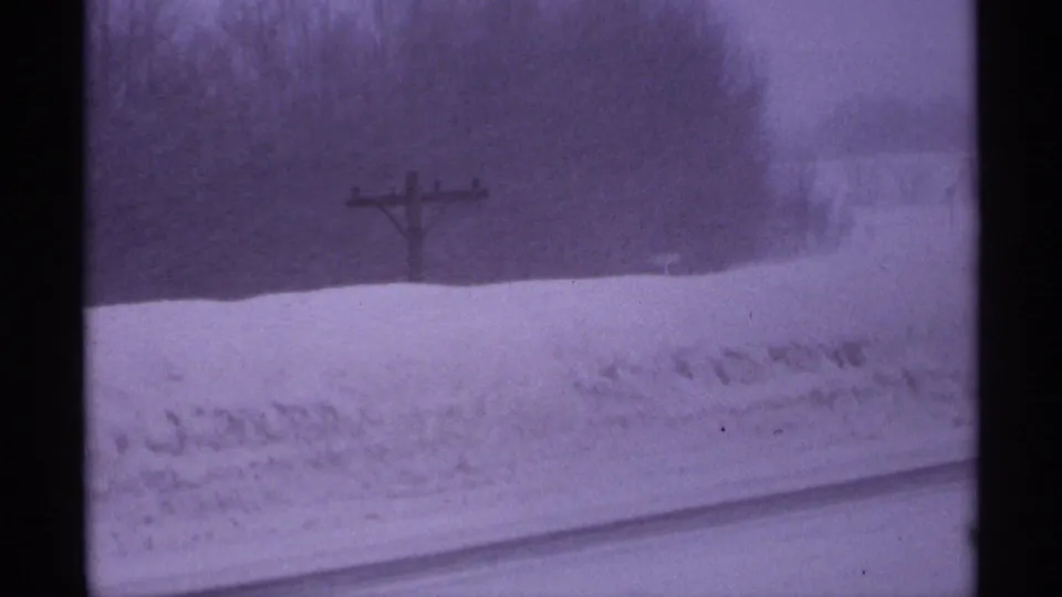 1971 Wisconsin home-movie frame with snowbanks, a wooden utility pole, distant trees, and visible film gate edges.
