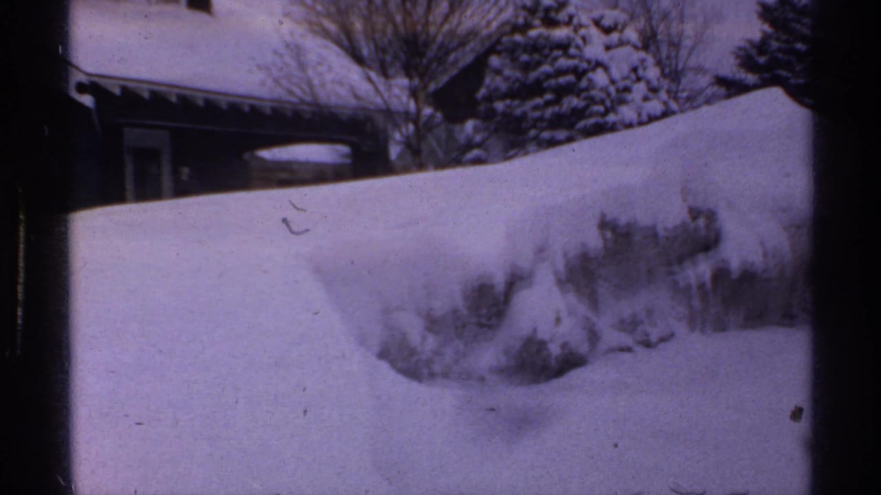 A snow-covered residential property in Wisconsin, 1971, with high drifts, trees, and a partially visible house.
