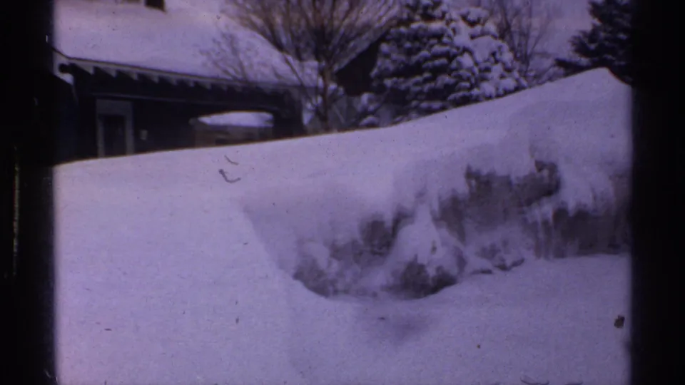 A snow-covered residential property in Wisconsin, 1971, with high drifts, trees, and a partially visible house.