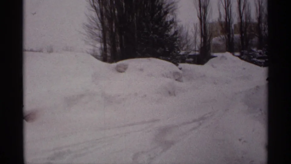 1971 Wisconsin 8mm frame showing a broad snowbank, leafless trees, evergreens, and a snow-covered rural area.