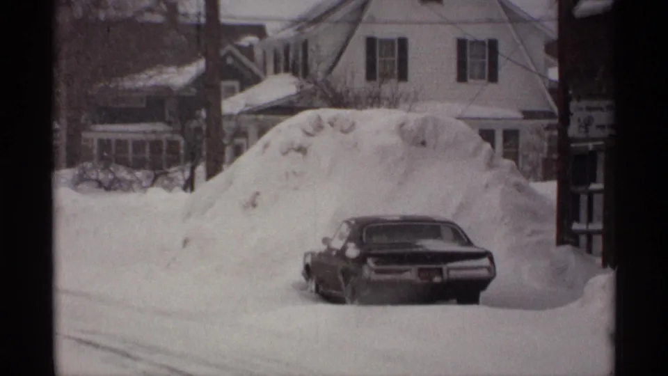 The same snowbound Wisconsin street shows a partly buried sedan, high plowed snow, houses, and overhead wires.