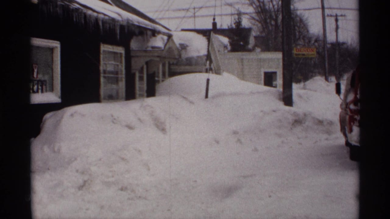 Residential snowbank beside houses with icicles and utility poles.