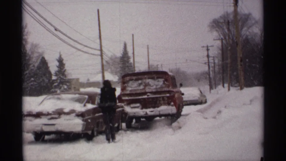 1971 Wisconsin winter frame with a buried sedan and red station wagon on a suburban road, with people standing in the snow.