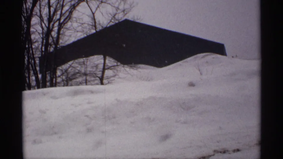 1971 Wisconsin 8mm frame showing a high snowbank, a dark-roofed house, and leafless trees in a residential winter setting.