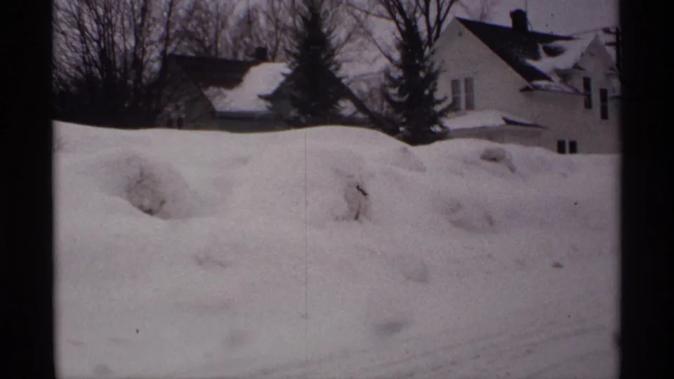 1971 Wisconsin 8mm frame of snow-covered homes and leafless trees beyond a broad foreground snowbank.