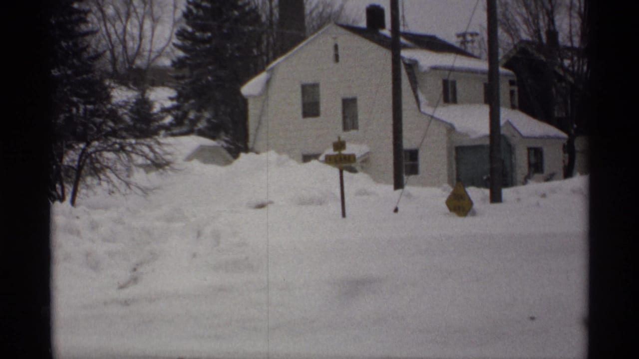Snow-covered house and road signs behind high winter drifts.