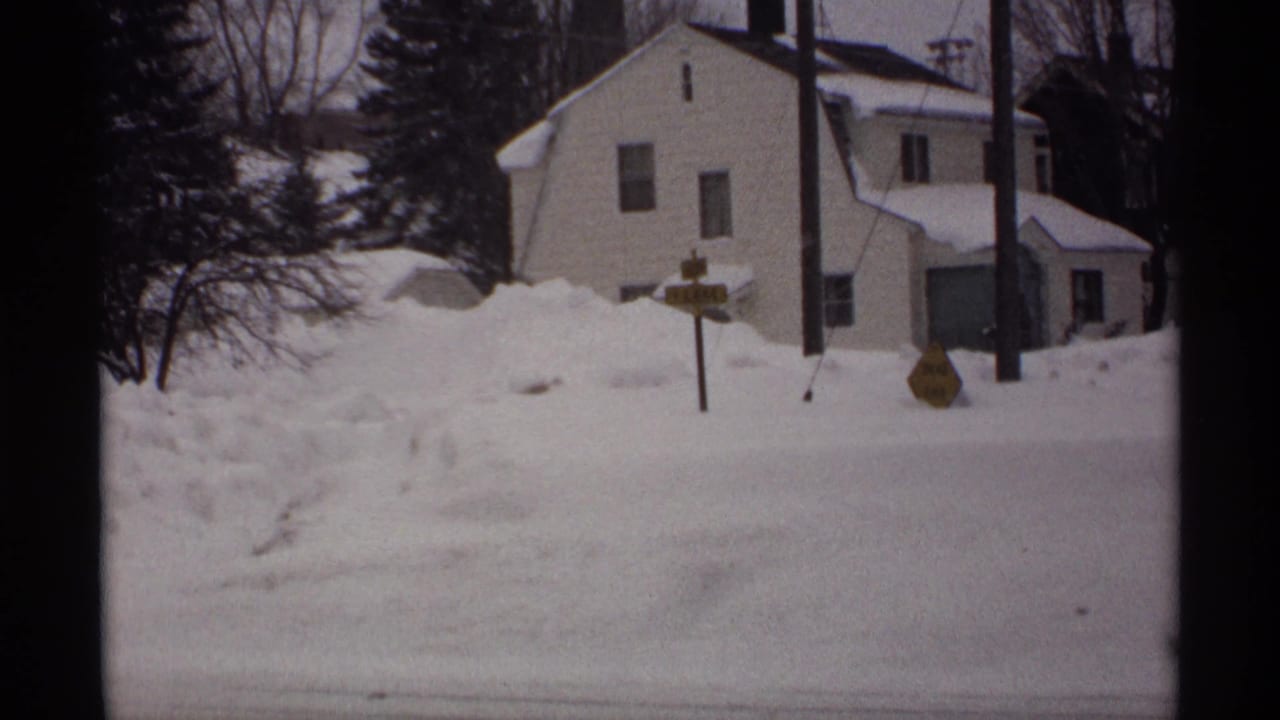 White house, roadside signs, and deep snow along a quiet street.