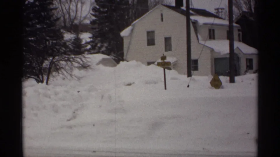 1971 Wisconsin 8mm frame of a quiet residential road edge with a white house and heavy snow accumulation.
