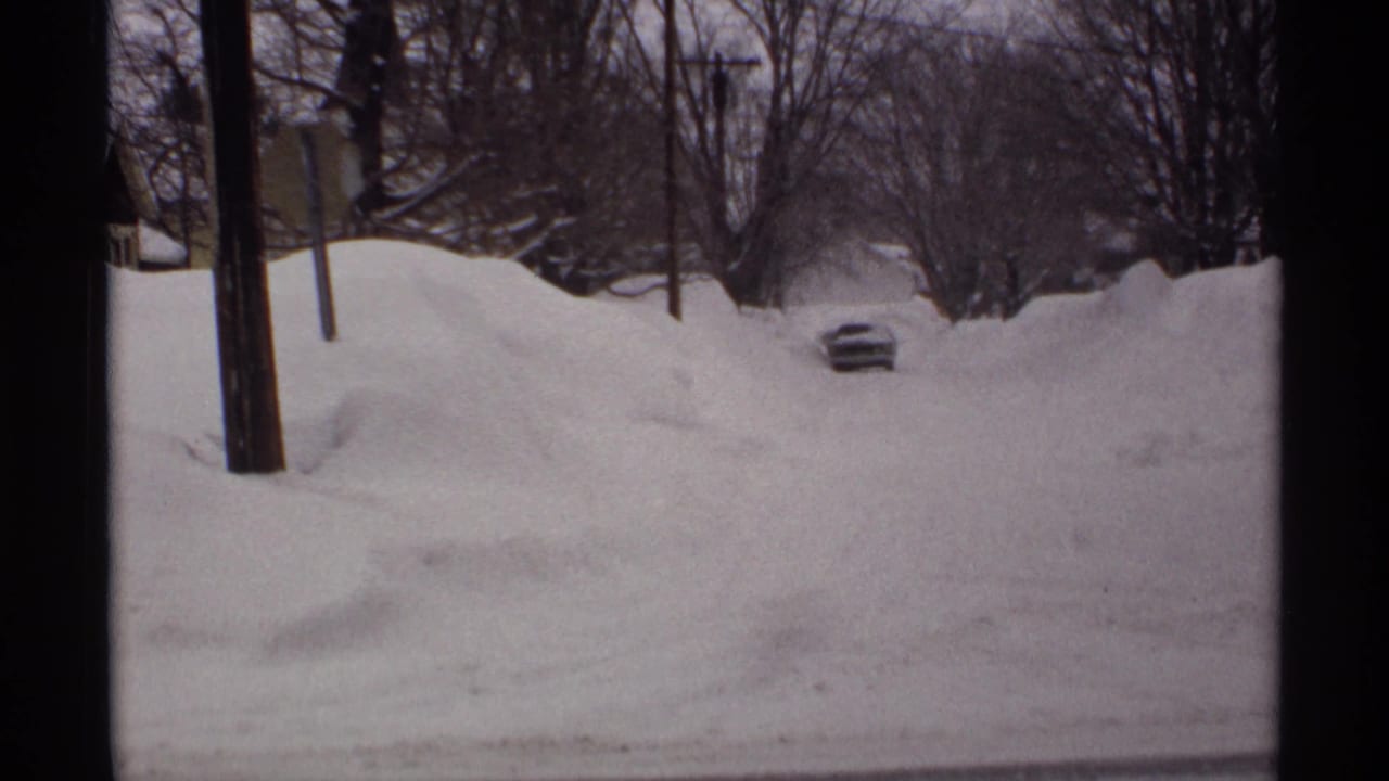 Snow-buried residential street with a car roof visible between high drifts.