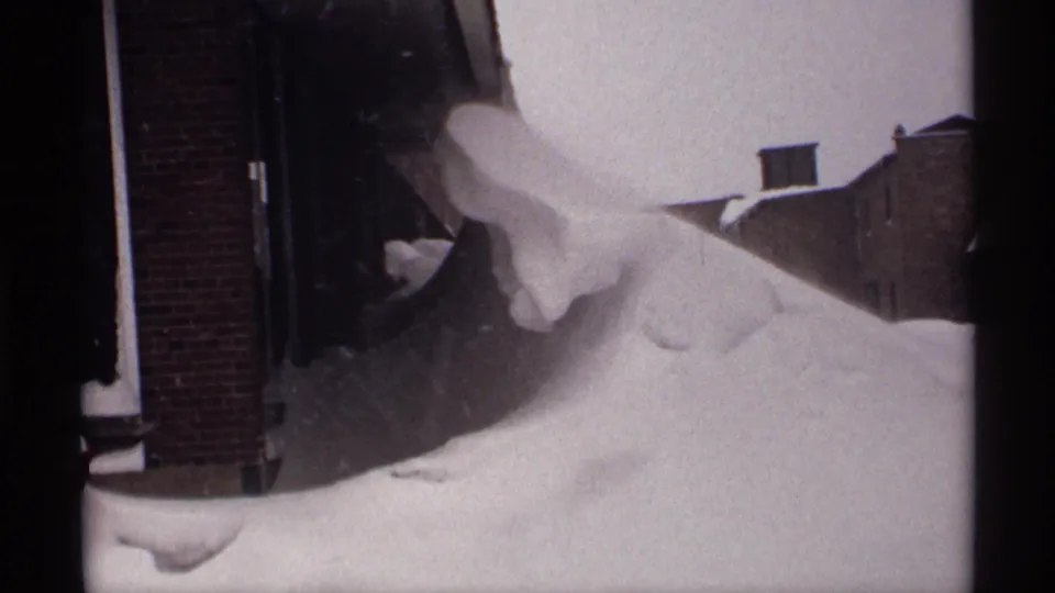 The final frame shows a sculpted snowdrift against a brick residential exterior, with neighboring walls visible beyond it.
