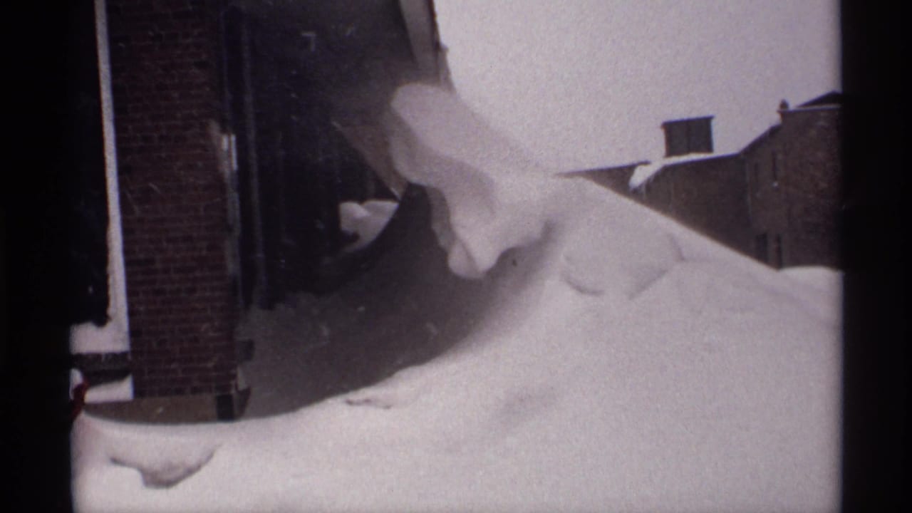 1971 Wisconsin 8mm frame showing snow heaped near brick residential buildings, with dark film borders and a narrow street view.