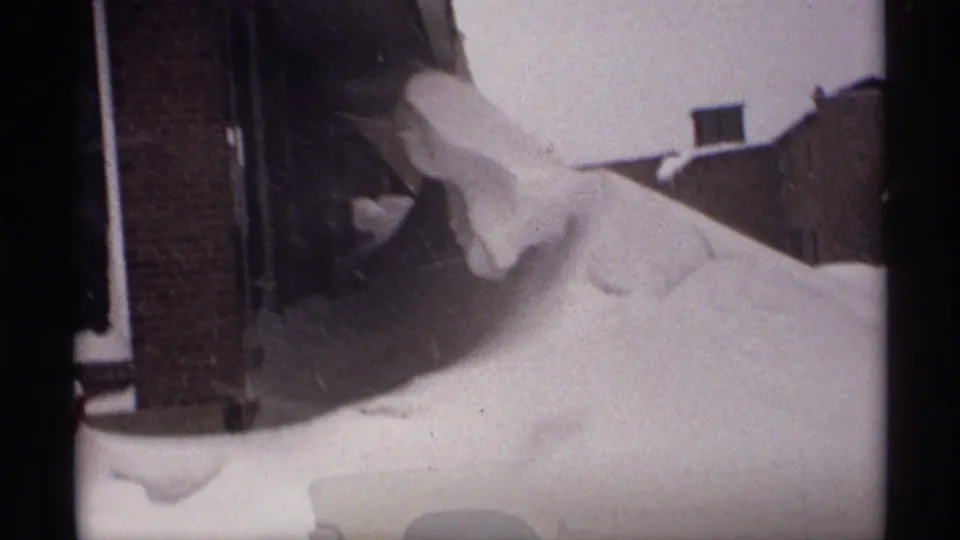 1971 Wisconsin frame with deep snowbanks around brick residences, seen through the soft grain and edge shadows of 8mm film.