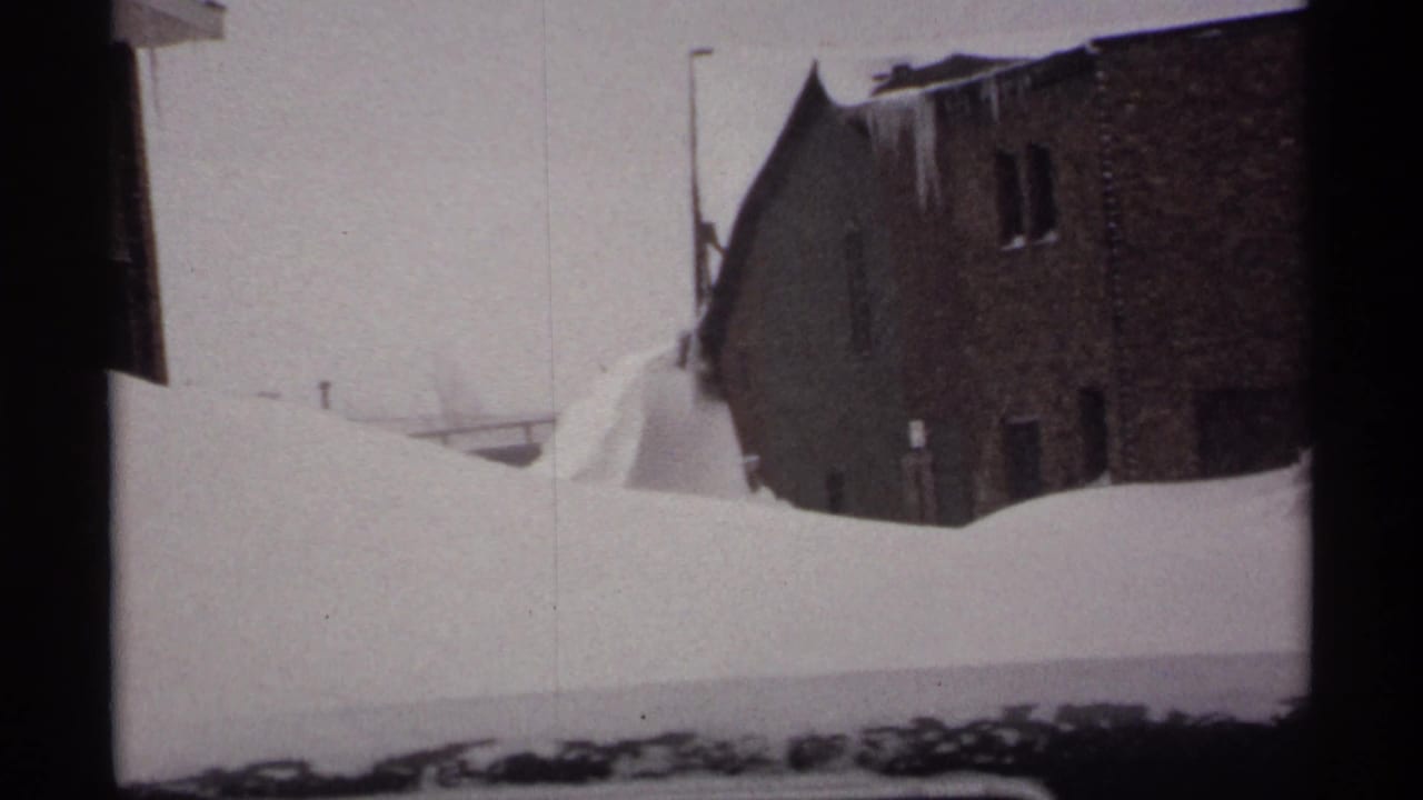 Tall snowbank between brick buildings with icicles along the roof edge.