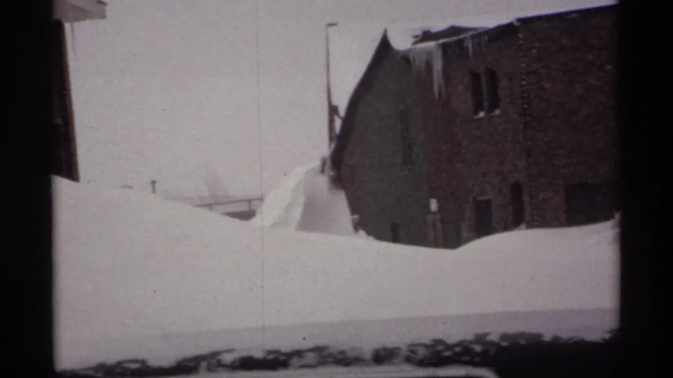 1971 Wisconsin home-movie view of deep snow piled between brick buildings, with icicles hanging from the eaves.